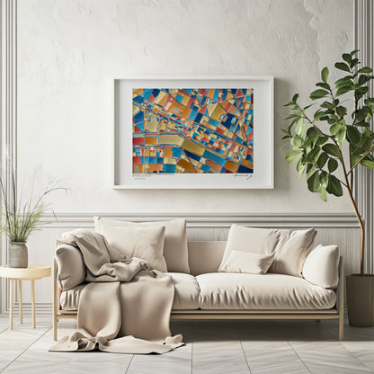 Affiche fine art représentant une carte géographique abstraite de la Place de la Concorde et du Jardin des Tuileries à Paris, dans des tons bleu, or, rouge et ocre, encadrée et accrochée au-dessus d’un canapé beige dans un intérieur élégant et lumineux.