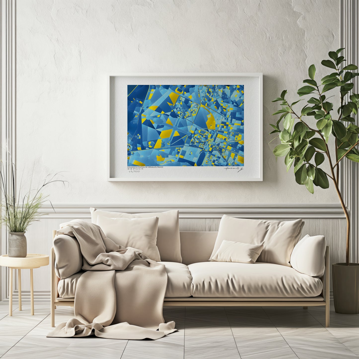 Carte abstraite bleue et jaune du Domaine du Château de Versailles, encadrée et accrochée au-dessus d’un canapé beige dans un intérieur lumineux et élégant.