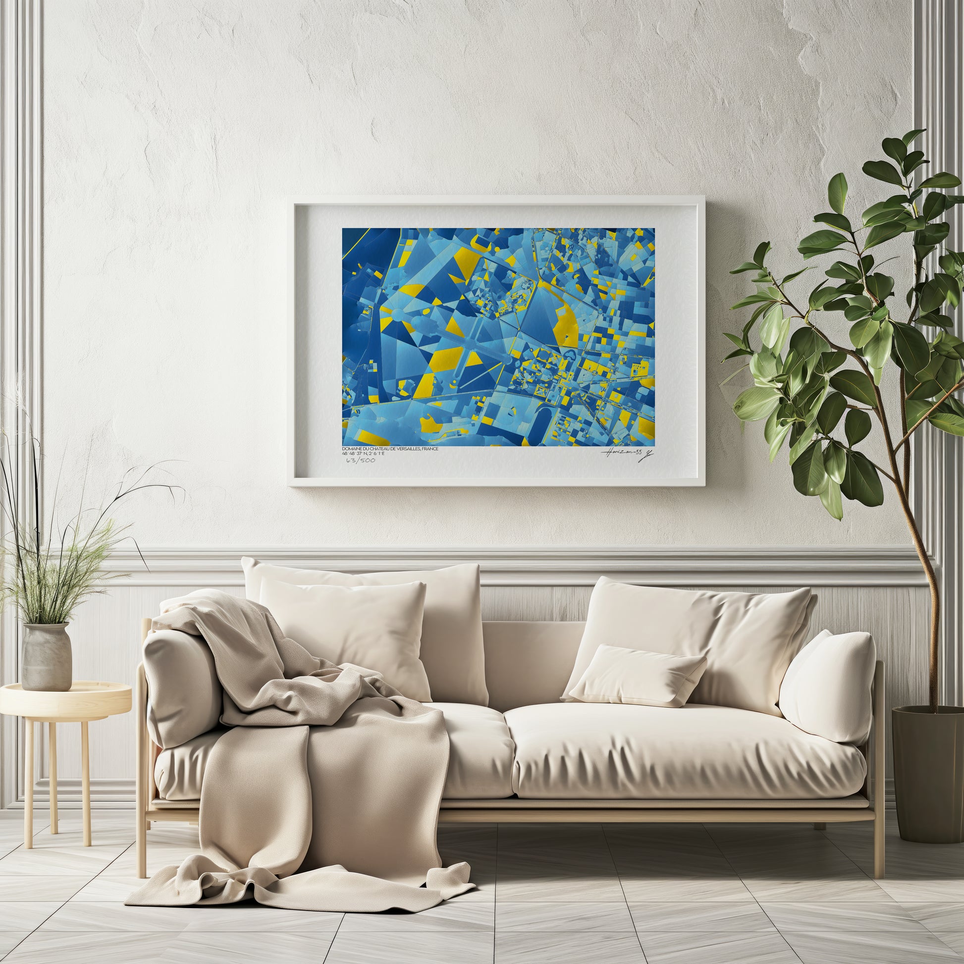 Carte abstraite bleue et jaune du Domaine du Château de Versailles, encadrée et accrochée au-dessus d’un canapé beige dans un intérieur lumineux et élégant.